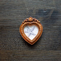 A heart-shaped wooden keepsake frame with an ornate copper-brown border, containing a white textured insert with a printed or painted starfish design, placed on a dark rustic wooden surface.